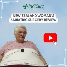 A headshot of a smiling elderly New Zealand woman named Rhoda. The image promotes her bariatric surgery review with IndiCure.